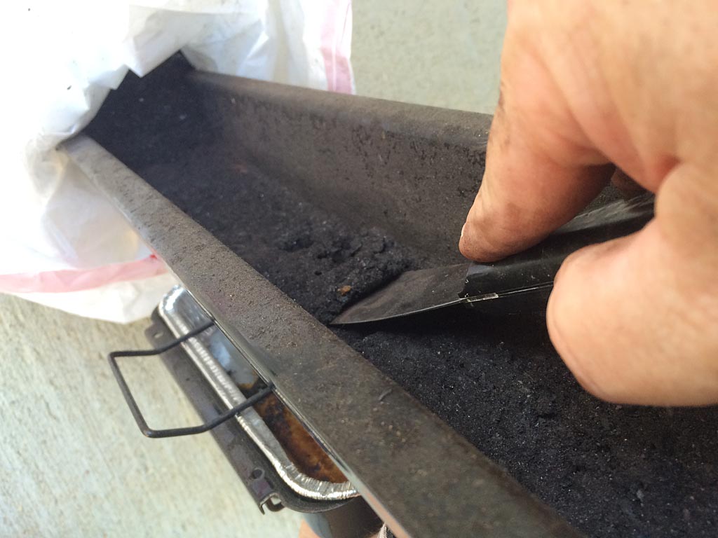 Scraping debris from bottom tray into a garbage bag