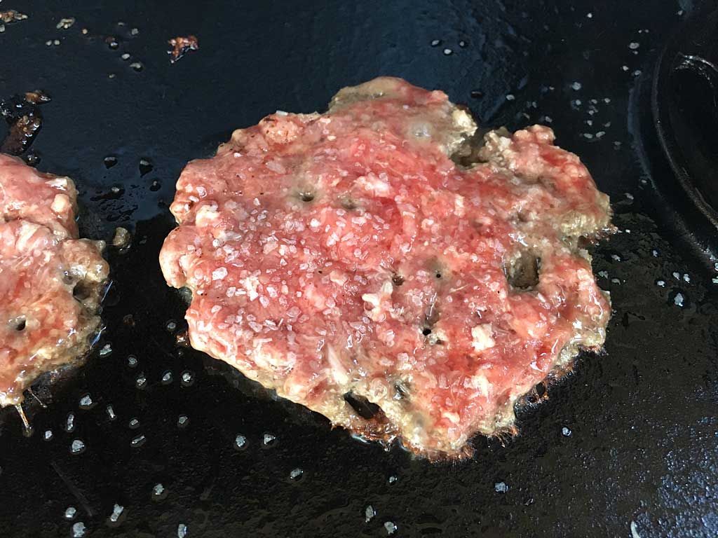 Close-up of smashed, seasoned burger patty before flipping