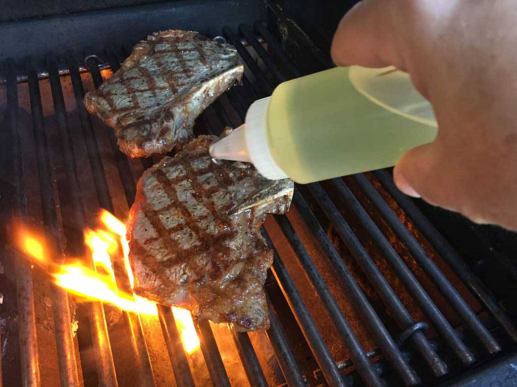 Applying a squirt of shallot oil to steaks while grilling